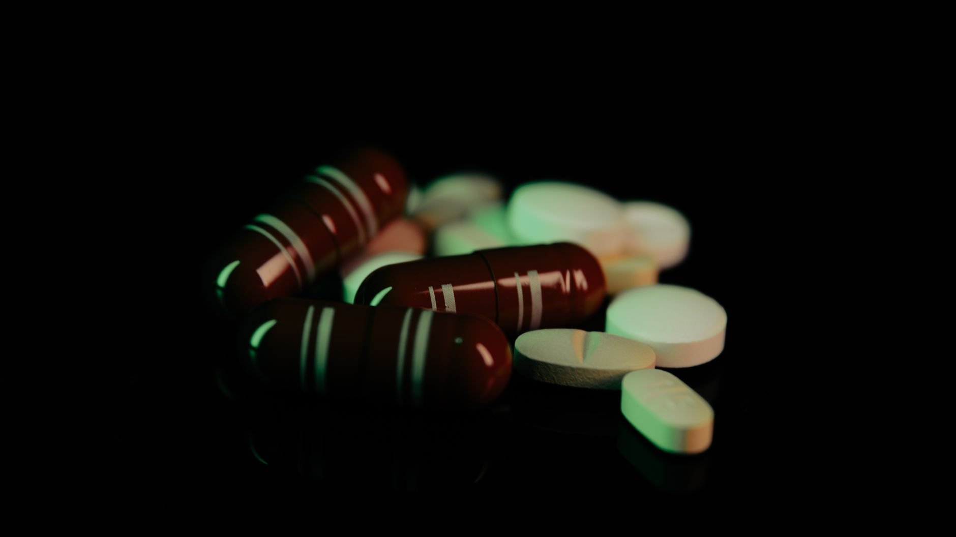 Assorted pills and capsules illuminated in green light on dark surface